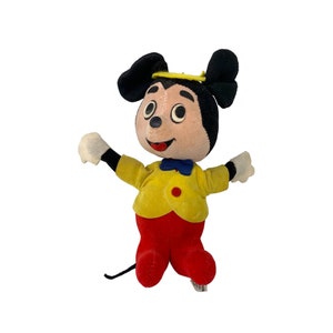 May include: A vintage plush Mickey Mouse toy wearing a yellow jacket, red pants, and a blue bow tie. The toy has a yellow halo and black ears.