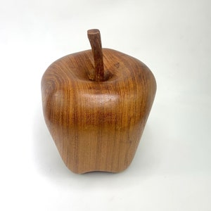 May include: A wooden apple sculpture with a brown finish. The apple is carved with a detailed stem and has a smooth, polished surface.
