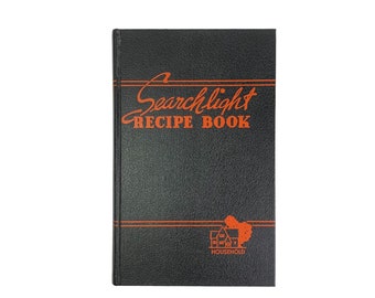May include: A black recipe book with the title "Searchlight Recipe Book" printed in orange on the front cover. The book also has a small orange illustration of a house with a tree next to it and the word "Household" printed below it.