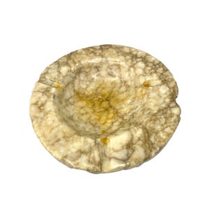 Op de afbeelding: Een ronde asbak met een gemarmerd patroon in tinten beige, bruin en geel. De asbak heeft een ondiepe komvorm met drie inkepingen om sigaretten op te leggen.