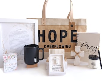 May include: A gift basket with a burlap tote bag that says "HOPE OVERFLOWING" and includes a black mug, a white framed print, a white cross, a white prayer journal, a small box with a white cross, a pack of prayer cards, and a small jar of hand cream.