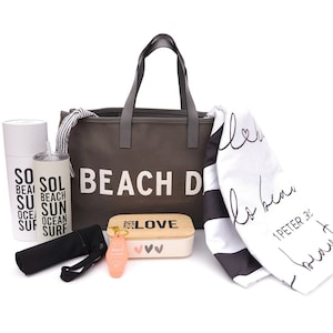 May include: A gray canvas tote bag with the text "Beach Days" printed on the front. The bag is filled with various items, including a white and black striped beach towel, a white tumbler with black text, a black and white lunch bag, and a pink keychain.
