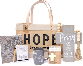 May include: A gift basket with a burlap tote bag that says "HOPE OVERFLOWING", a gray mug with the text "Be still and know", a gray journal with a leaf pattern, a small gray notebook with a leaf pattern, a wooden cross with the text "Pray let go and let God take over", a small white card with a cross and the text "a prayer for you", and a wooden bead garland.