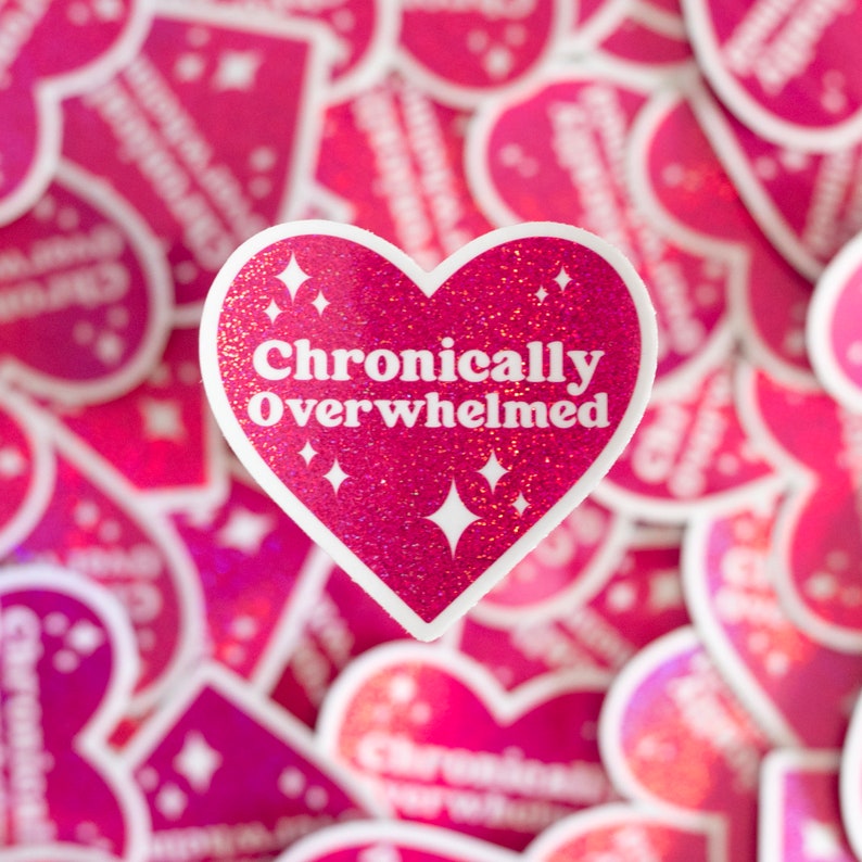 Pode incluir: Adesivo rosa em forma de cora&ccedil;&atilde;o com glitter e texto branco que diz "Cronicamente sobrecarregado".