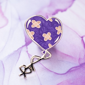 May include: Purple heart-shaped balloon with a silver string and pink band-aid designs. The balloon is a pin.