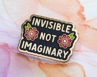 May include: Gold enamel pin with a black background and white text that reads "Invisible Not Imaginary". The pin is decorated with two purple and green flowers.