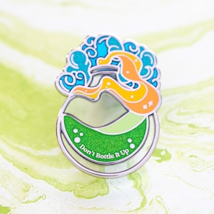 Puede incluir: Pin esmaltado plateado con diseño de botella de poción. La botella contiene líquido verde y el texto "Don't Bottle It Up". El diseño incluye detalles en azul, naranja y amarillo, con un elemento en forma de nube arremolinada encima de la botella.