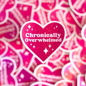 Pode incluir: Adesivo rosa em forma de cora&ccedil;&atilde;o com glitter e o texto "Cronicamente Sobrecarregado" em branco.