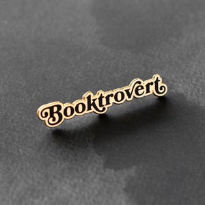 May include: Gold-colored pin with the word "Booktrovert" in black lettering.