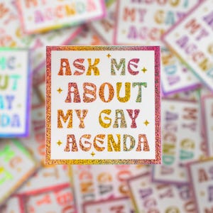 May include: A rainbow glitter sticker with the text "Ask Me About My Gay Agenda".