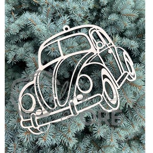 May include: A light-colored wooden cutout ornament shaped like a classic rounded car. The design features open-work detailing for the windows, wheels, and body panels, with a small hole at the top for hanging. The surface has a natural wood grain.