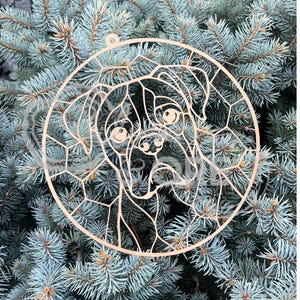 May include: A circular light-colored wooden ornament featuring a laser-cut geometric design of a boxer dog face. The intricate cutout pattern forms the shape of the dog's head, ears, and snout within a thin circular frame with a small hanging loop.