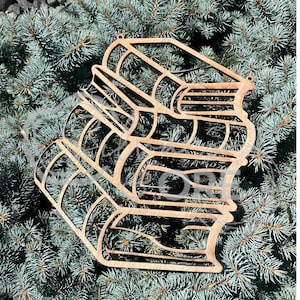 May include: A laser-cut wooden ornament shaped like a stack of three books. The design features intricate cutouts defining the covers and pages of each book, with a small hole at the top for hanging. The natural light brown wood grain is visible.