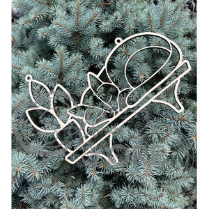 May include: A light-colored, laser-cut wooden ornament featuring a stylized fox resting on a branch, surrounded by leaf-shaped cutouts. The design includes a small circular hole at the top for hanging, with clean, smooth edges and a natural wood finish.