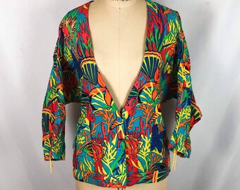 May include: A colorful, open-front blouse with a vibrant underwater-themed print. The fabric features a mix of red, blue, green, and yellow coral and sea life patterns. The blouse has long sleeves and is displayed on a mannequin.