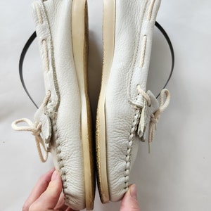 Puede incluir: Un par de zapatos n&aacute;uticos de cuero blanco con cordones. Los zapatos est&aacute;n usados y tienen una suela de color crema.