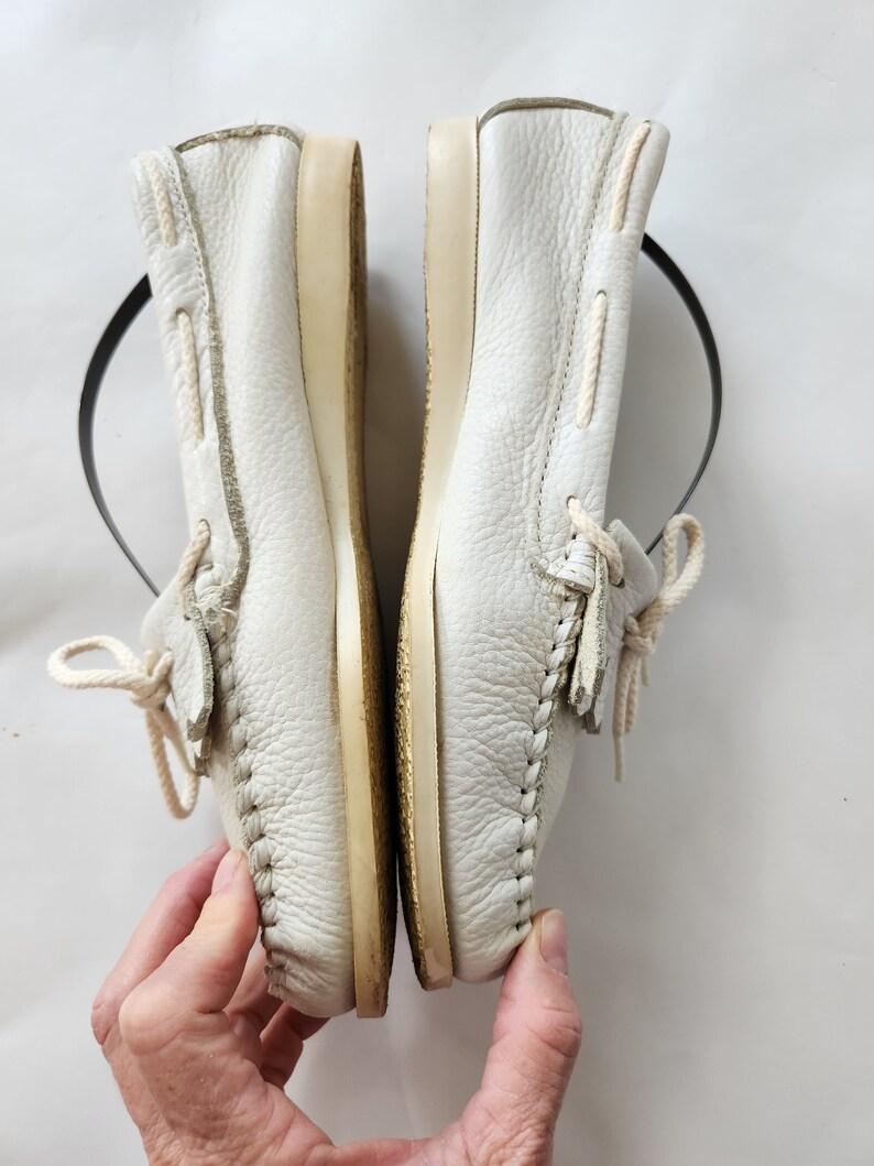 Puede incluir: Un par de zapatos n&aacute;uticos de cuero blanco con cordones. Los zapatos est&aacute;n usados y tienen una suela de color crema.