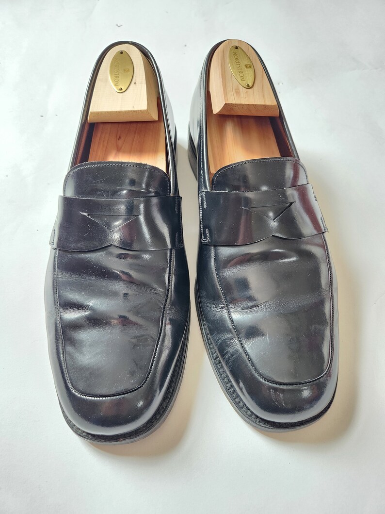May include: A pair of black leather loafers with a simple design. The loafers have a rounded toe and a slip-on style. The shoes are on a white background.