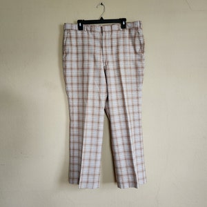 May include: Brown and white plaid pants hanging on a hanger against a beige wall.
