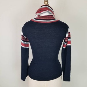 May include: A navy blue long-sleeved shirt with a striped turtleneck collar. The stripes are red, white, and gray.