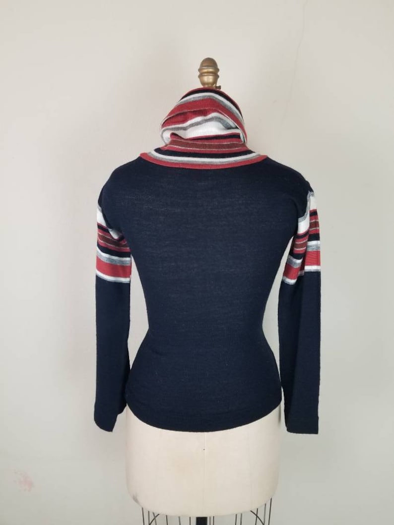 May include: A navy blue long-sleeved shirt with a striped turtleneck collar. The stripes are red, white, and gray.