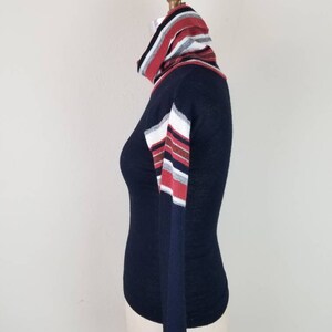 May include: A navy blue long-sleeved turtleneck sweater with red, white, and gray striped detailing on the sleeves and collar.