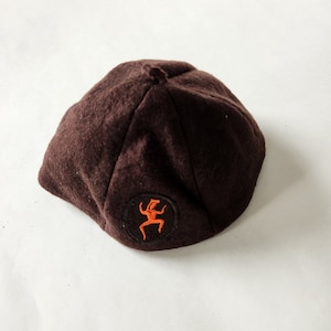 May include: A brown felt beret with an orange embroidered design of a stylized figure dancing.