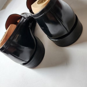 May include: A pair of black leather loafers with wooden shoe trees inside. The loafers have a polished finish and a rounded toe.