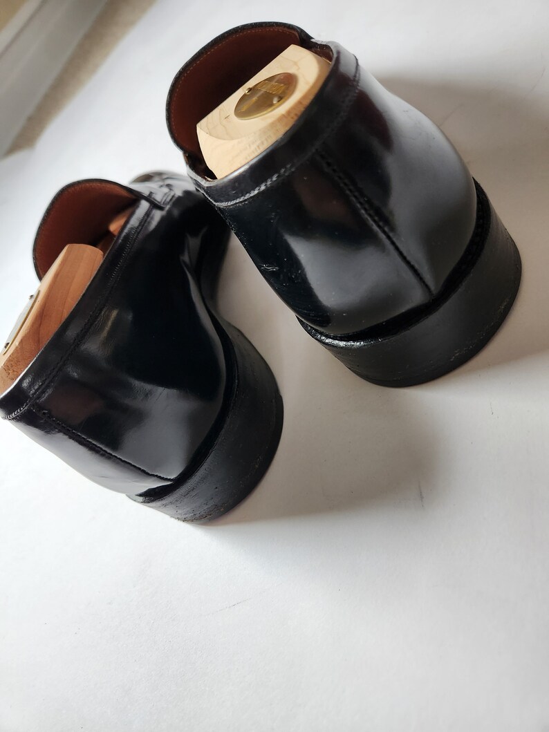 May include: A pair of black leather loafers with wooden shoe trees inside. The loafers have a polished finish and a rounded toe.