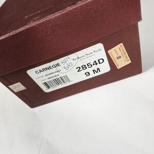 May include: A brown shoe box with a white label that says "CARNEGIE 324" and "To Boot New York ADAM DERRICK". The label also includes the text "ROANO/CALF", "NERO/BLK", "2854D", and "9 M".