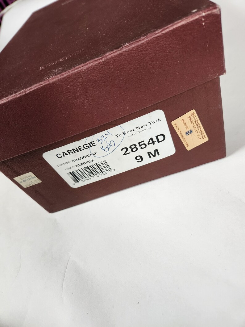 May include: A brown shoe box with a white label that says "CARNEGIE 324" and "To Boot New York ADAM DERRICK". The label also includes the text "ROANO/CALF", "NERO/BLK", "2854D", and "9 M".