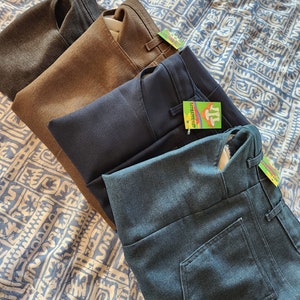 May include: Four pairs of pants folded on top of each other. The pants are in different colors: gray, brown, navy blue, and dark blue. The pants are all made of a similar fabric and have a similar style.