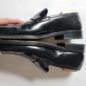 May include: A pair of black leather loafers with a buckle detail. The loafers are stacked on top of each other.