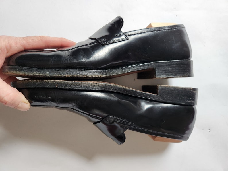 May include: A pair of black leather loafers with a buckle detail. The loafers are stacked on top of each other.