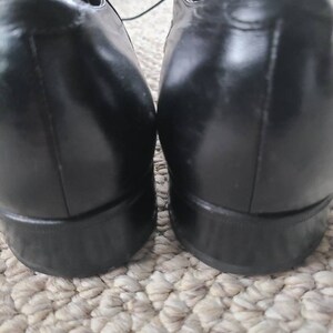 May include: A pair of black leather dress shoes. The shoes have a glossy finish and a classic design, with laces visible at the top. The heels are a solid, dark color.
