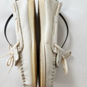 Puede incluir: Un par de zapatos n&aacute;uticos de cuero blanco con cordones blancos. Los zapatos est&aacute;n colocados uno al lado del otro con las suelas mirando hacia el espectador.