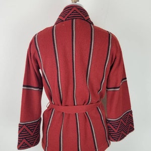 May include: A red and black striped knit cardigan with a geometric pattern on the collar and cuffs. The cardigan has a belt.