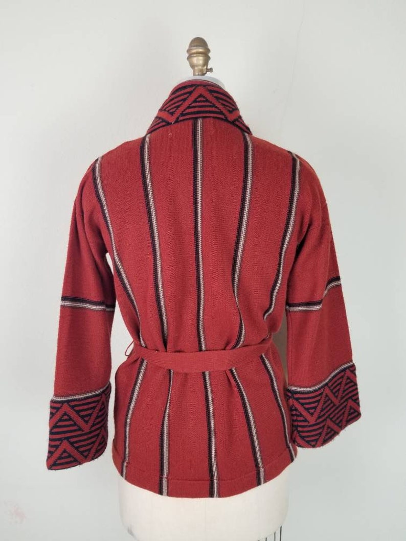 May include: A red and black striped knit cardigan with a geometric pattern on the collar and cuffs. The cardigan has a belt.