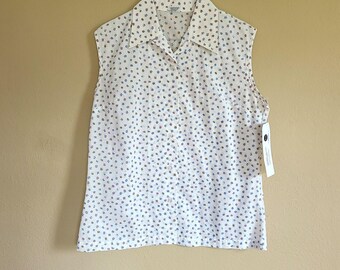 May include: White sleeveless blouse with a small blue and red floral pattern. The collared shirt is button-down and hangs on a metal hanger. A price tag is attached to the bottom of the shirt.