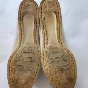 Puede incluir: Primer plano de la parte inferior de un par de zapatos de cuero blanco con suela de goma texturizada.
