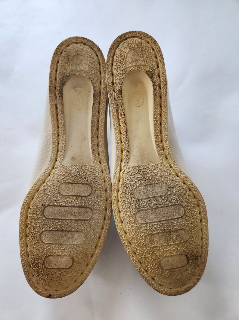 Puede incluir: Primer plano de la parte inferior de un par de zapatos de cuero blanco con suela de goma texturizada.