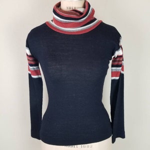 May include: Black turtleneck sweater with red, white, and gray striped sleeves.
