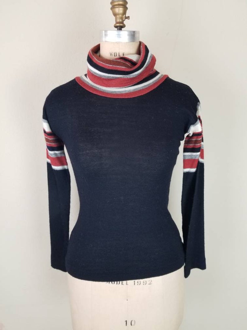 May include: Black turtleneck sweater with red, white, and gray striped sleeves.