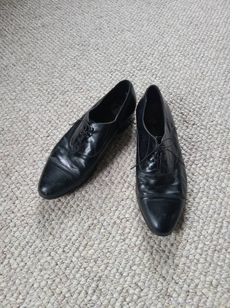 May include: A pair of black leather dress shoes with laces. The shoes have a classic design with a pointed toe and a low heel. The leather appears to be slightly worn, giving them a vintage look.