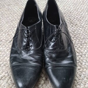 May include: A pair of black leather dress shoes with laces. The shoes have a classic design with a rounded toe and a low heel. The leather appears worn, with visible creases and scuffs, suggesting regular use.