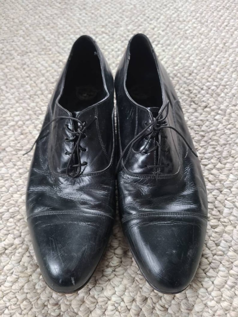 May include: A pair of black leather dress shoes with laces. The shoes have a classic design with a rounded toe and a low heel. The leather appears worn, with visible creases and scuffs, suggesting regular use.