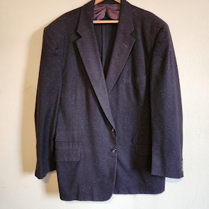 May include: A dark gray blazer with a single button closure. The blazer has a pocket on the left chest and two flap pockets on the bottom.