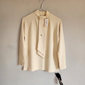 May include: A pale yellow sweater with a mock neck and a long tie detail. The sweater has a tag that says "Talbott".