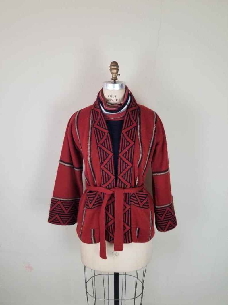 May include: A red, black, and white patterned cardigan with a tie belt. The cardigan has a geometric design and is made of a soft, knit fabric.