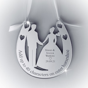 May include: A silver horseshoe-shaped wedding ornament with a bride and groom silhouette. The ornament has the text "Add up to 40 characters on outer horseshoe" and "Shaun & Jessica Watkins 29.09.21" engraved on it.
